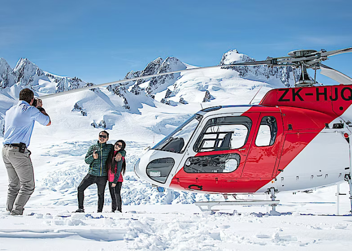 Glacier Helicopters A Pilot Taking Photos Of Two Customers On A Snow Landing